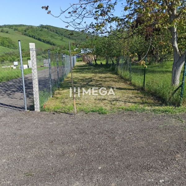 Pozemek na bydlení v Humenném na oplocené ulici, obklopený zelení.