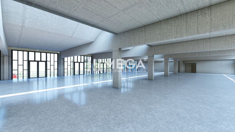 Velká prosklená hala v obchodních prostorách s betonovými sloupy a hladkou podlahou.