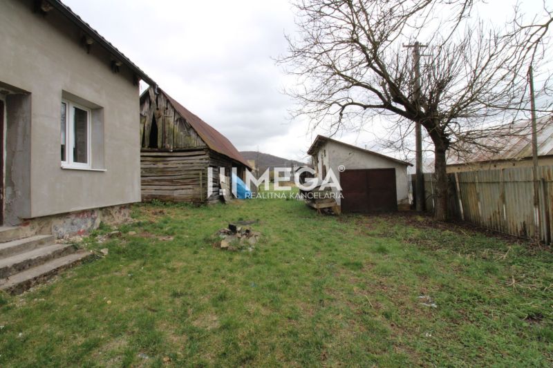 Zahrada u rodinného domu na ulici v Pakostově, se starší dřevěnou kůlnou a trávníkem.