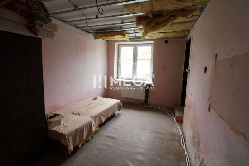 Nezařízený interiér rodinného domu s postelí a odkrytým stropem.