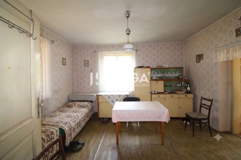 Pokoj v rodinném domě s tapetami, stolem, postelí, vitrínou a podlahou s dřevěným dekorem.