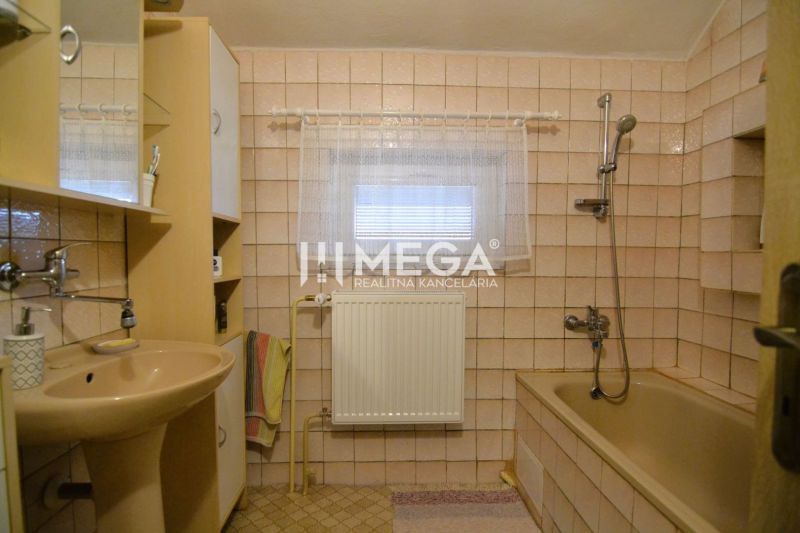 Koupelna v rodinném domě s béžovým obkladem, vanou a umyvadlem.