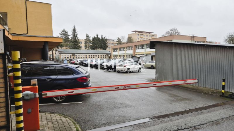 Parkoviště před kancelářemi na ulici 26. listopadu v Humenném se závorou a auty.