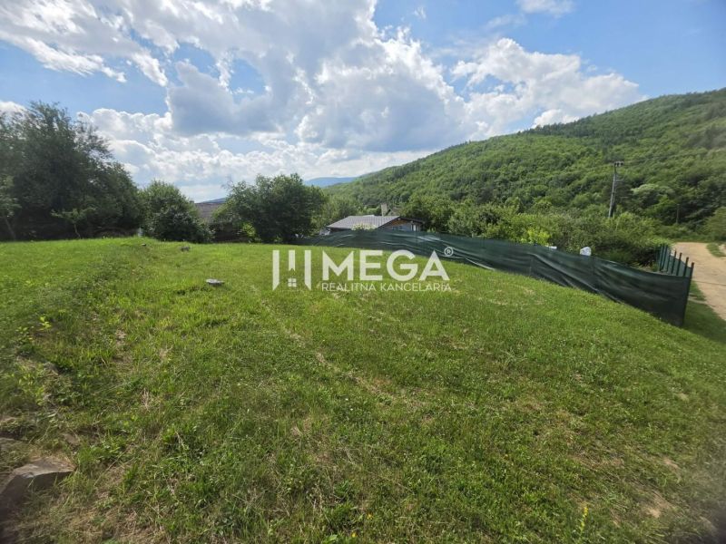 Zahrady se zeleným trávníkem v Snině na ulici Snina obklopené lesnatými kopci.