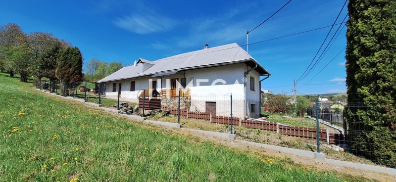 Rodinný dům v obci Zbudská Belá obklopený zelenými trávníky a stromy.