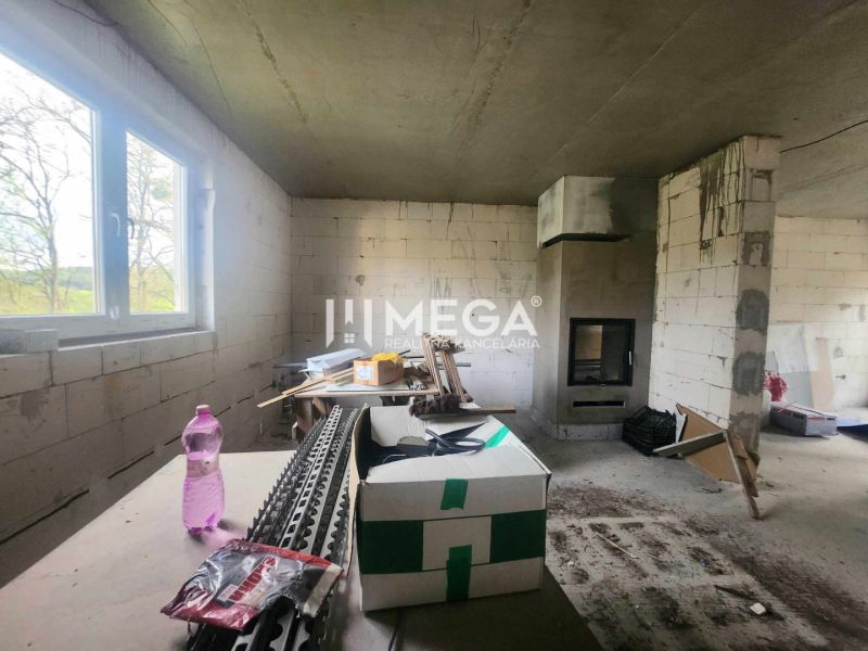 Interiér rodinného domu s nedokončenými stěnami, krbem a stavebním materiálem.
