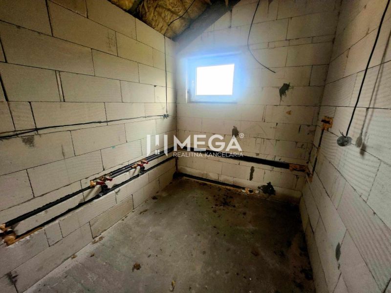 Interiér rodinného domu s betonovou podlahou, cihlovými stěnami a malým oknem.