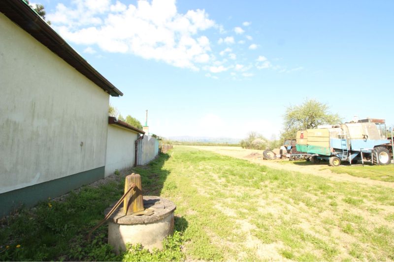 Exteriér v Sačurově pro Pozemky - bydlení s budovou, zemědělským strojem a studnou.