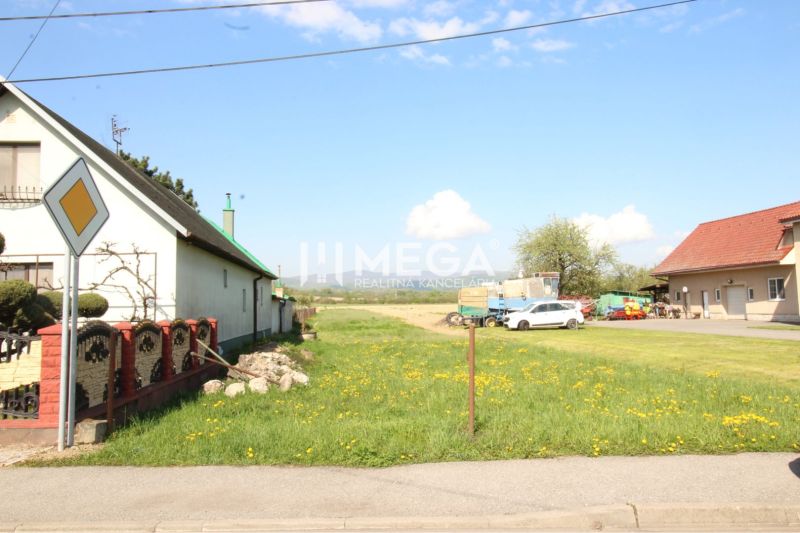 Pozemky - bydlení v Sačurově s domy, trávníkem a dopravní značkou.