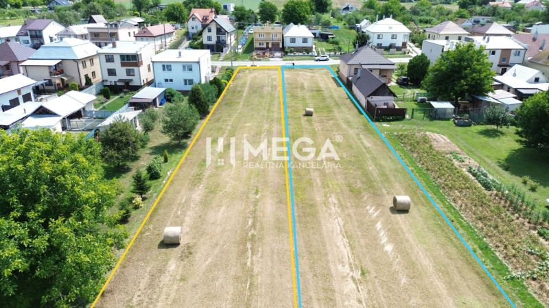Pozemky - bydlení v Jasenově obklopené domy a zelenými stromy.