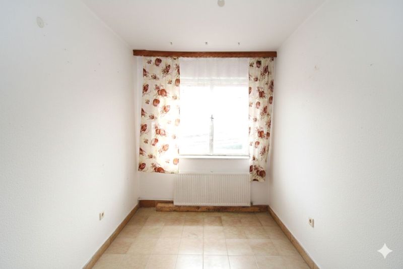 Pokoj v rodinném domě s oknem, květinové záclony a dlažba.