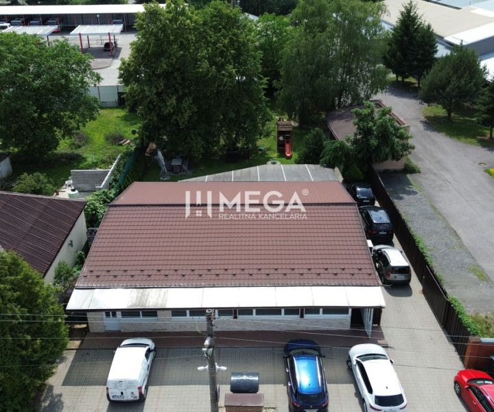 Gastro prostory na Budovatelské ulici ve Vranově nad Topľou obklopené auty a zelení.