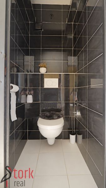 Koupelna v 3-pokojovém bytě s tmavě šedými obklady a bílou sanitou.