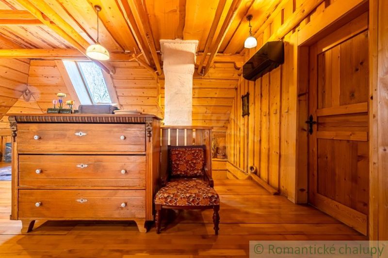 Podkroví rodinného domu se skříní, křeslem a podlahou s dřevěným dekorem.