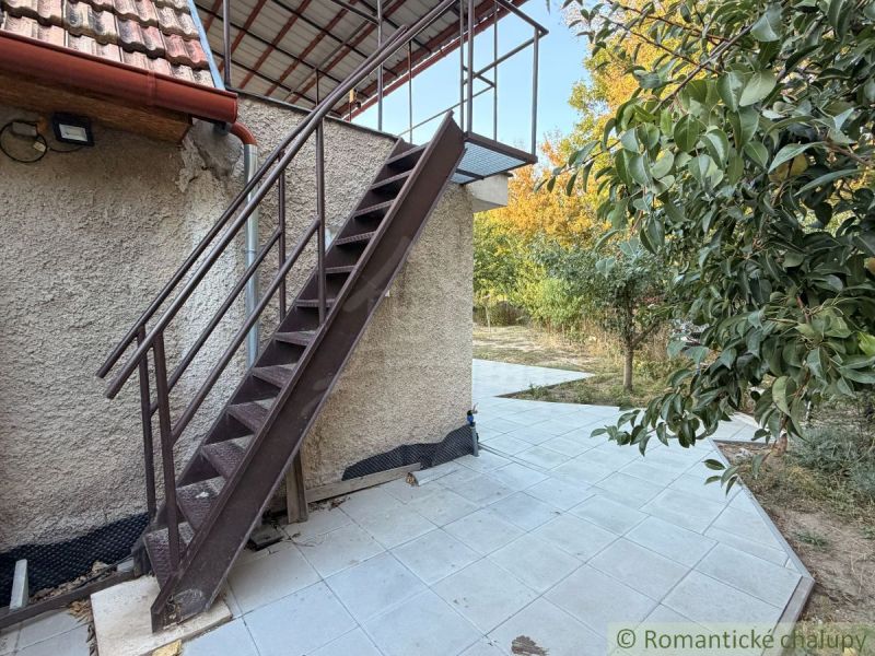 Exteriér chaty v Nových Zámcích s kovovým schodištěm a terasou obklopenou zelení.