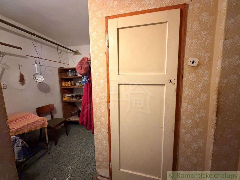 Interiér rodinného domu s předsíní, židlí a regály. Visí tu kuchyňské nástroje.