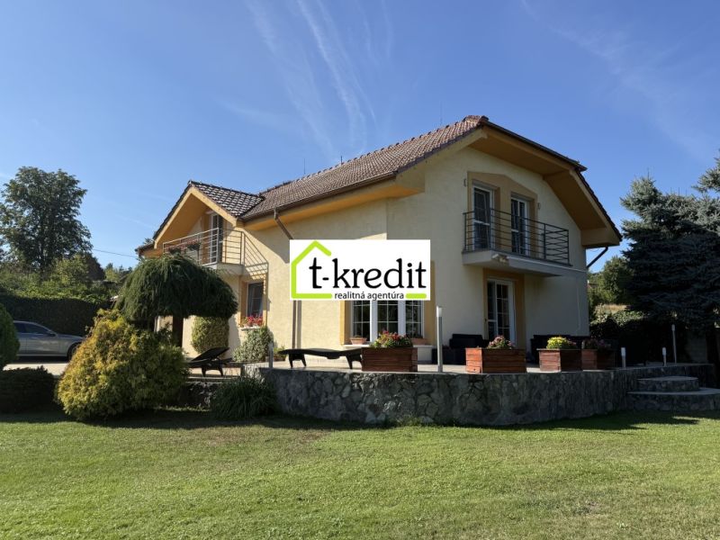 Rodinný dům ve Zlatých Moravcích, obklopený zelení, s kamennou terasou a balkónem.