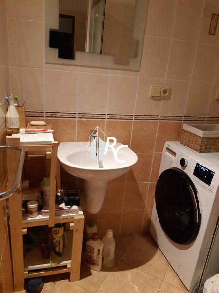Koupelna se zrcadlem a pračkou v 2-pokojovém bytě s béžovými obklady.