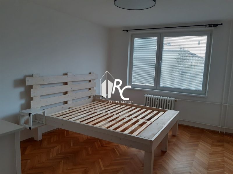 Světlá ložnice s dřevěnou postelí a podlahou s dřevěným dekorem v 2-pokojovém bytě.