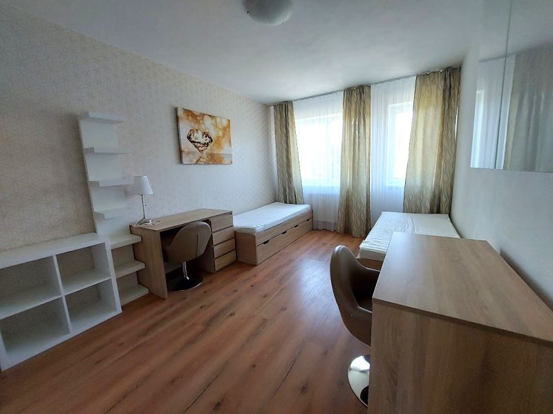 Pokoj s dvěma postelemi, stoly a podlahou s dřevěným dekorem v 3-pokojovém bytě.