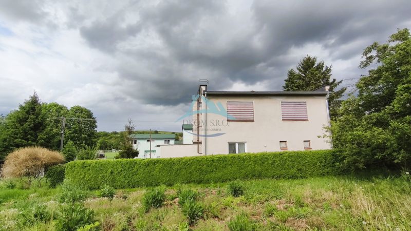Rodinný dům v Neninciach obklopený hustou zelení a stromy pod zamračenou oblohou.
