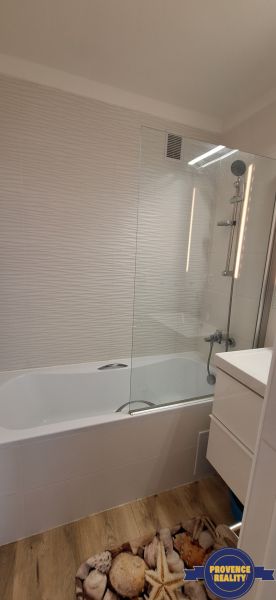 Koupelna v 3-pokojovém bytě s vanou, bílými obklady a podlahou s dřevěným dekorem.