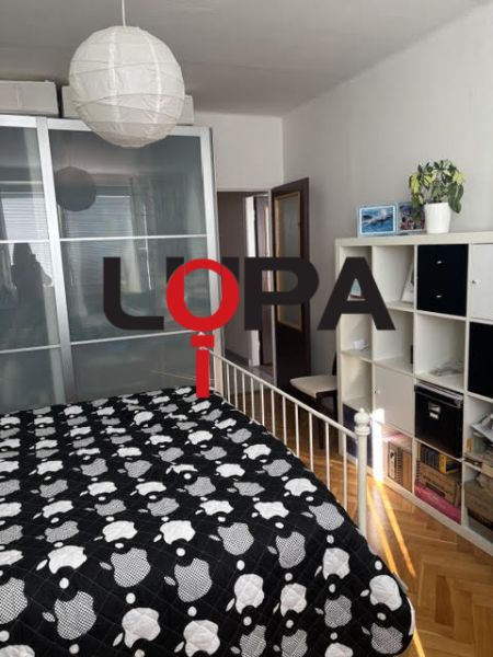 Ložnice v 2pokojovém bytě s úložným prostorem, postelí a podlahou s dřevěným dekorem.