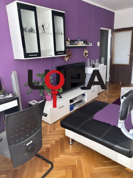 Obývací pokoj v 2-pokojovém bytě s pohovkou a nábytkem, podlaha s dřevěným dekorem.