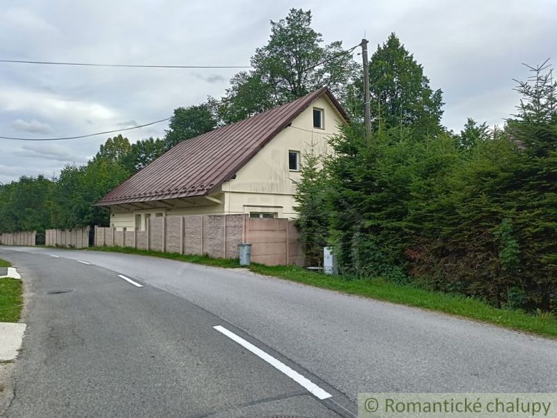 Rodinný dům ve Staškově s plechovou střechou, obklopený stromy a oplocením.