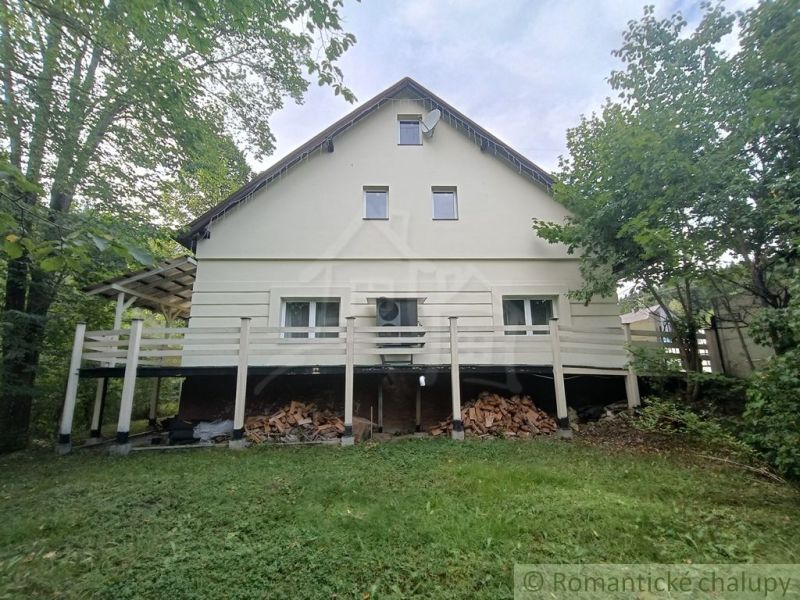 Rodinný dům ve Staškově, obklopený zelení, s dřevem uskladněným pod terasou.