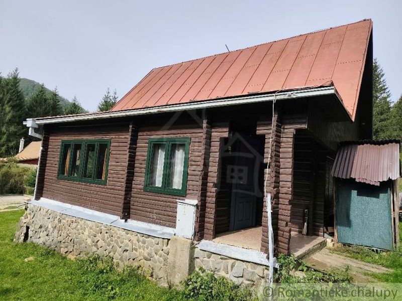 Dřevěná chata s plechovou střechou v přírodě Rajecké Lesné, obklopená zelení.