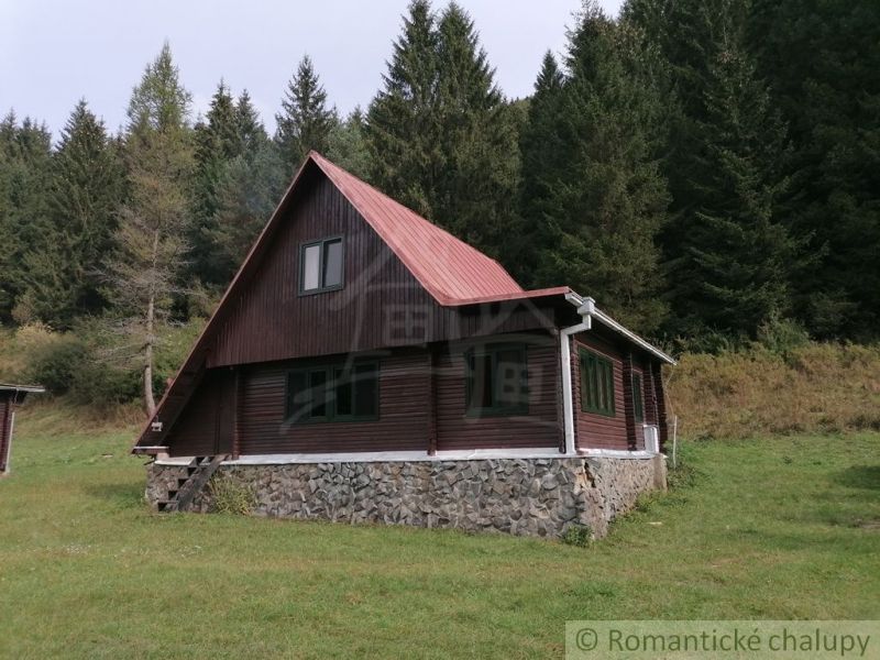 Chata v Rajecké Lesné obklopená lesem, s kamenným základem a střechou.