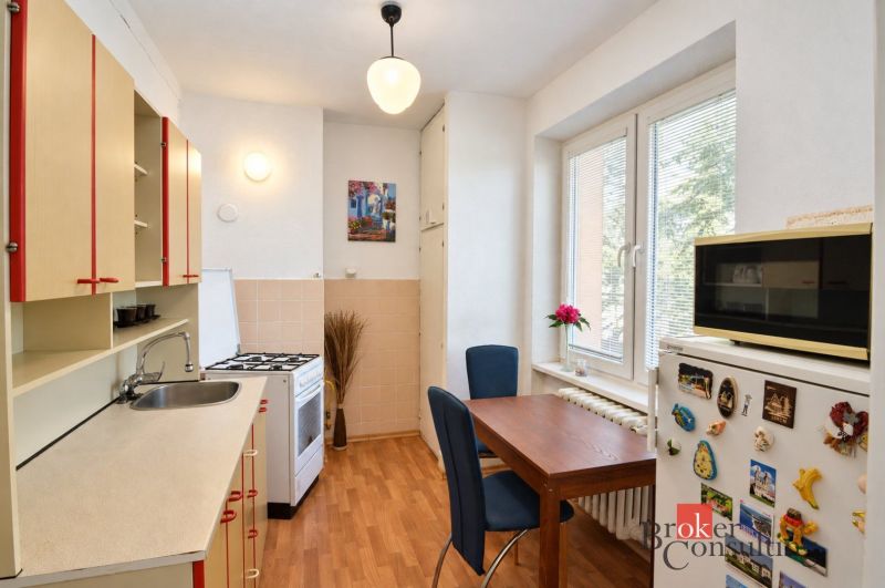 Kuchyně v 2-pokojovém bytě s podlahou s dřevěným dekorem, jídelním stolem a moderním vybavením.