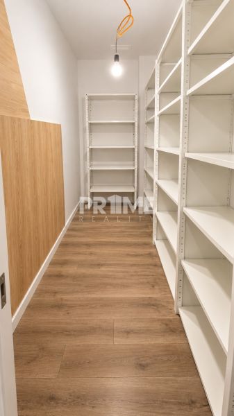 Úložný prostor s bílými regály a podlahou s dřevěným dekorem v 2-pokojovém bytě.