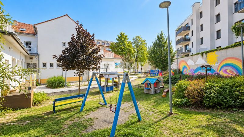 Dětské hřiště obklopené budovami s barevnými nástěnnými malbami na Sancově ulici.