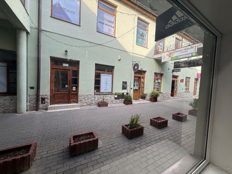 Obchodní prostory v Topoľčanech s kamenným obkladem a květináči na dlážděné ulici.