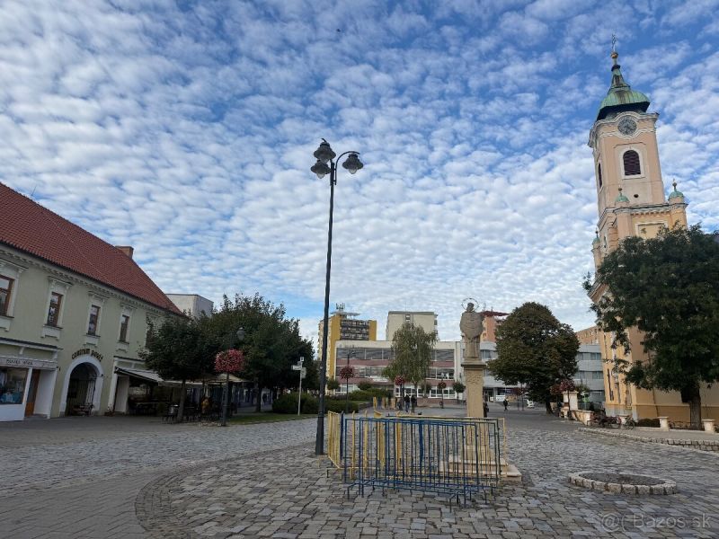 Obchodní prostory v Topoľčanech s dlážděným náměstím a kostelem v pozadí.