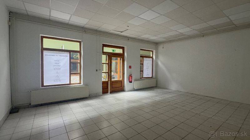 Obchodní prostory s dlažbou a velkými okny, čekající na využití.