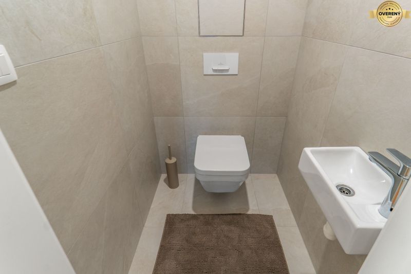 Toaleta se závěsným WC, malým umyvadlem a béžovou dlažbou, Výstavba bytů.
