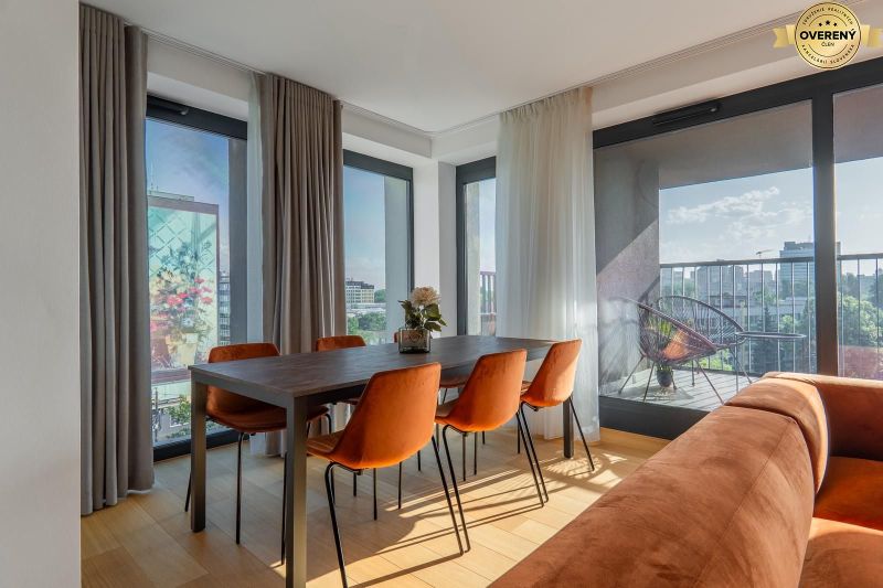 Jídelní kout s oranžovými židlemi, podlaha s dřevěným dekorem, výstup na balkon. Výstavba bytů.
