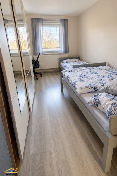 Pokoj s dvěma postelemi a podlahou s dřevěným dekorem v rodinném domě.