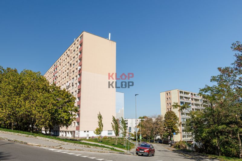 Bytové domy na Adámiho ulici v Bratislavě - Karlově Vsi obklopené zelení a cestou.