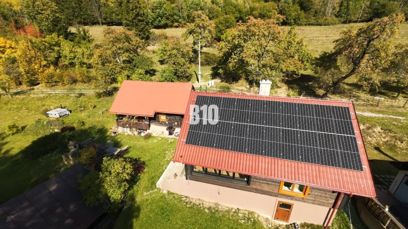 Dřevěná chata v Dlouhém Poli se solárními panely, obklopená zelení a přírodou.