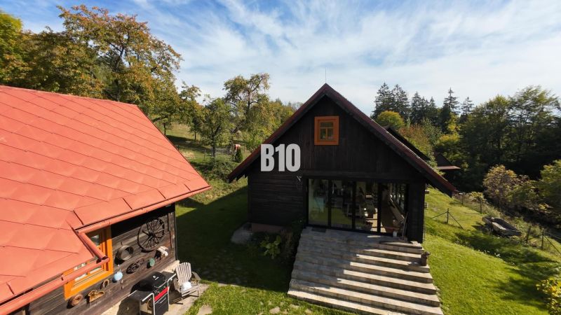 Chata v Dlhém Poli obklopená zelení s červenou střechou a terasou.