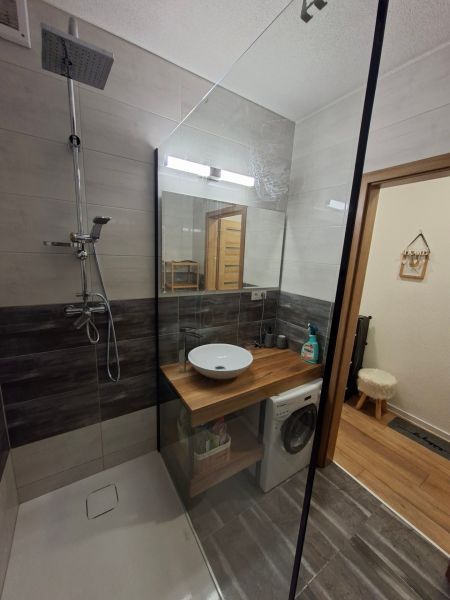 Koupelna s umyvadlem, sprchovým koutem a pračkou v 1-pokojovém bytě, podlaha s dřevěným dekorem.