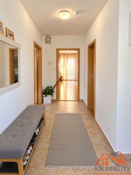 Chodba v rodinném domě s dlažbou, lavičkou na boty a zrcadlem.