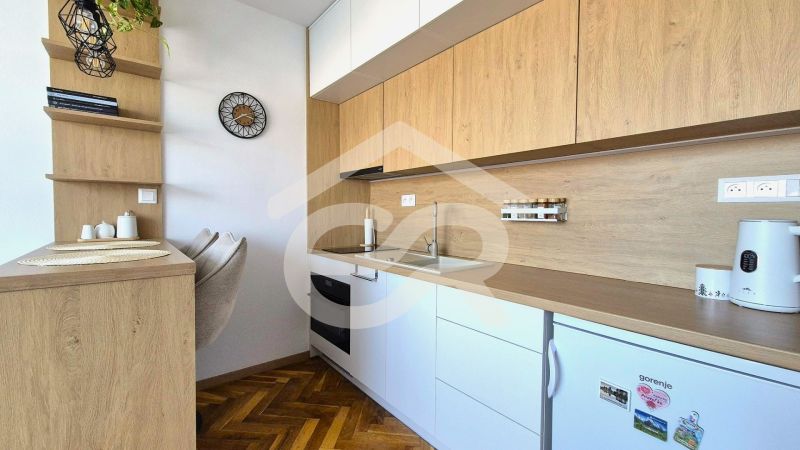 Kuchyňská linka v garsonce s podlahou s dřevěným dekorem a zabudovanými spotřebiči.