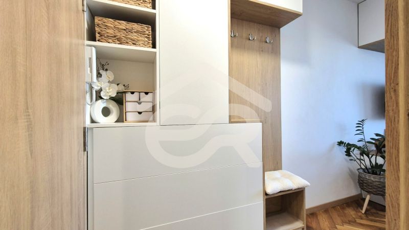 Interiér garsonky s dřevěným nábytkem, dekoracemi a rostlinou na podlaze s dřevěným dekorem.