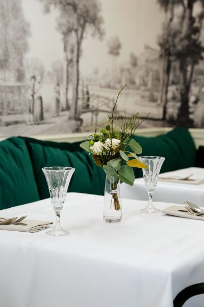 Elegantně prostřený stůl s bílým ubrusem, vázou s květinami a křišťálovými sklenicemi.