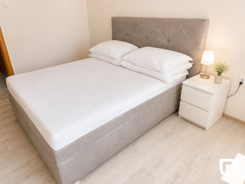 Postel s nočním stolkem a lampou v 2-pokojovém bytě na podlaze s dřevěným dekorem.